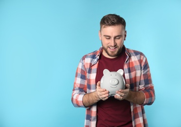 Photo of Happy young man with piggy bank and space for text on color background. Money saving