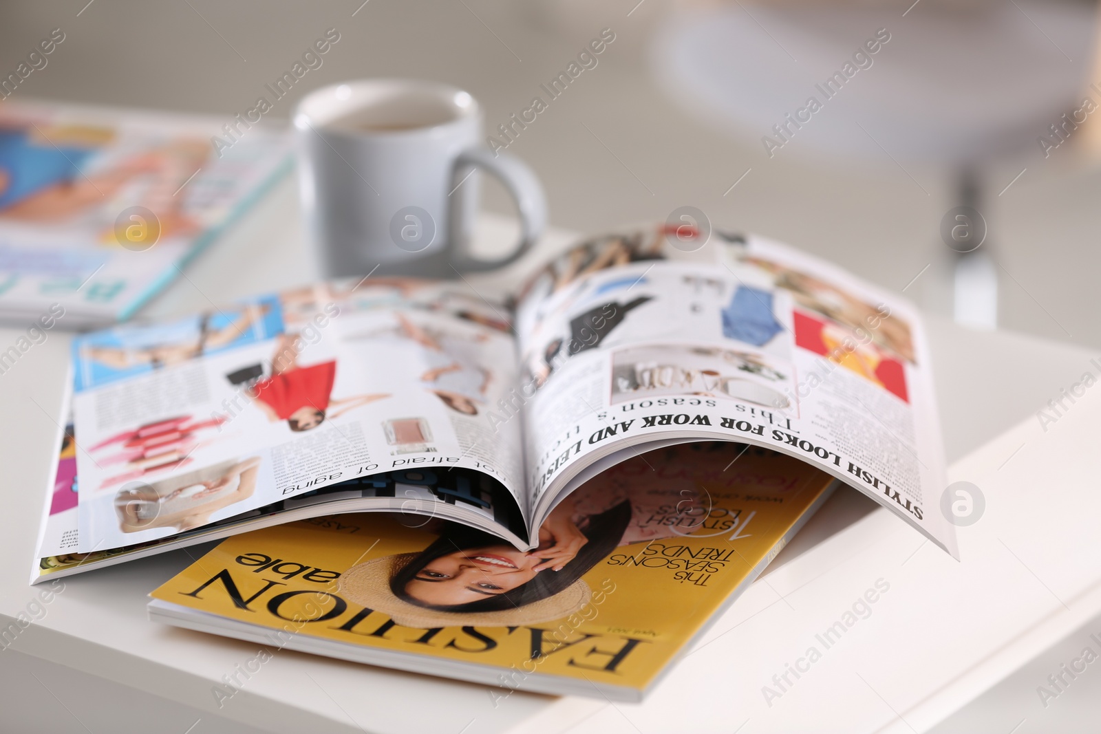 Photo of Fashion magazines and cup of hot drink on white table indoors, closeup