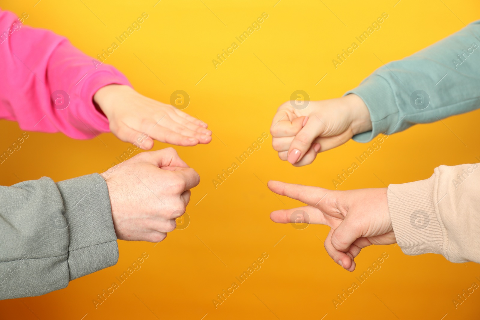 Photo of People playing rock, paper and scissors on orange background, closeup