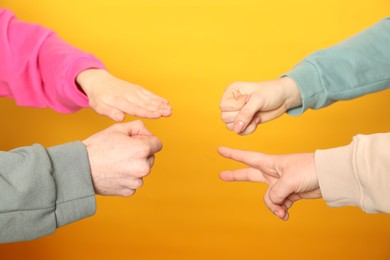 People playing rock, paper and scissors on orange background, closeup