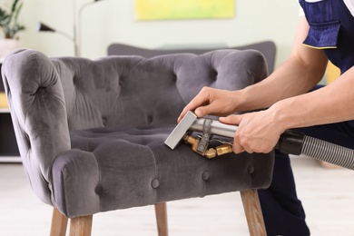 Photo of Male worker removing dirt from armchair with professional vacuum cleaner indoors, closeup