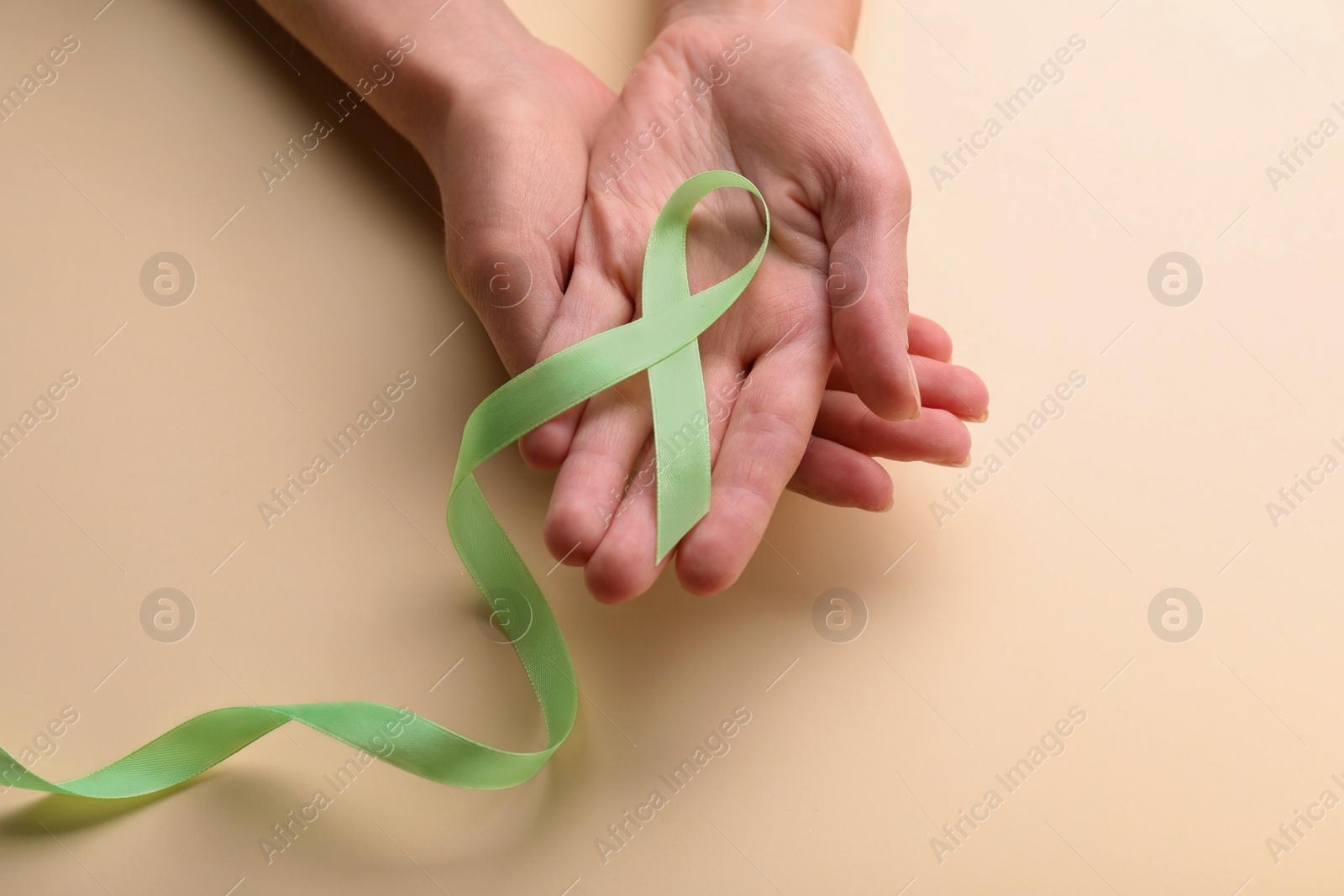 Photo of World Mental Health Day. Woman holding green ribbon on color background, top view