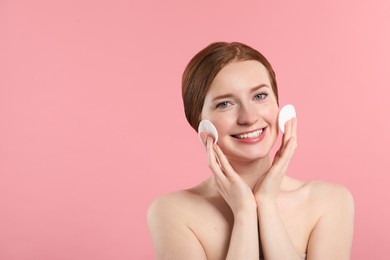 Smiling woman with freckles wiping face on pink background. Space for text