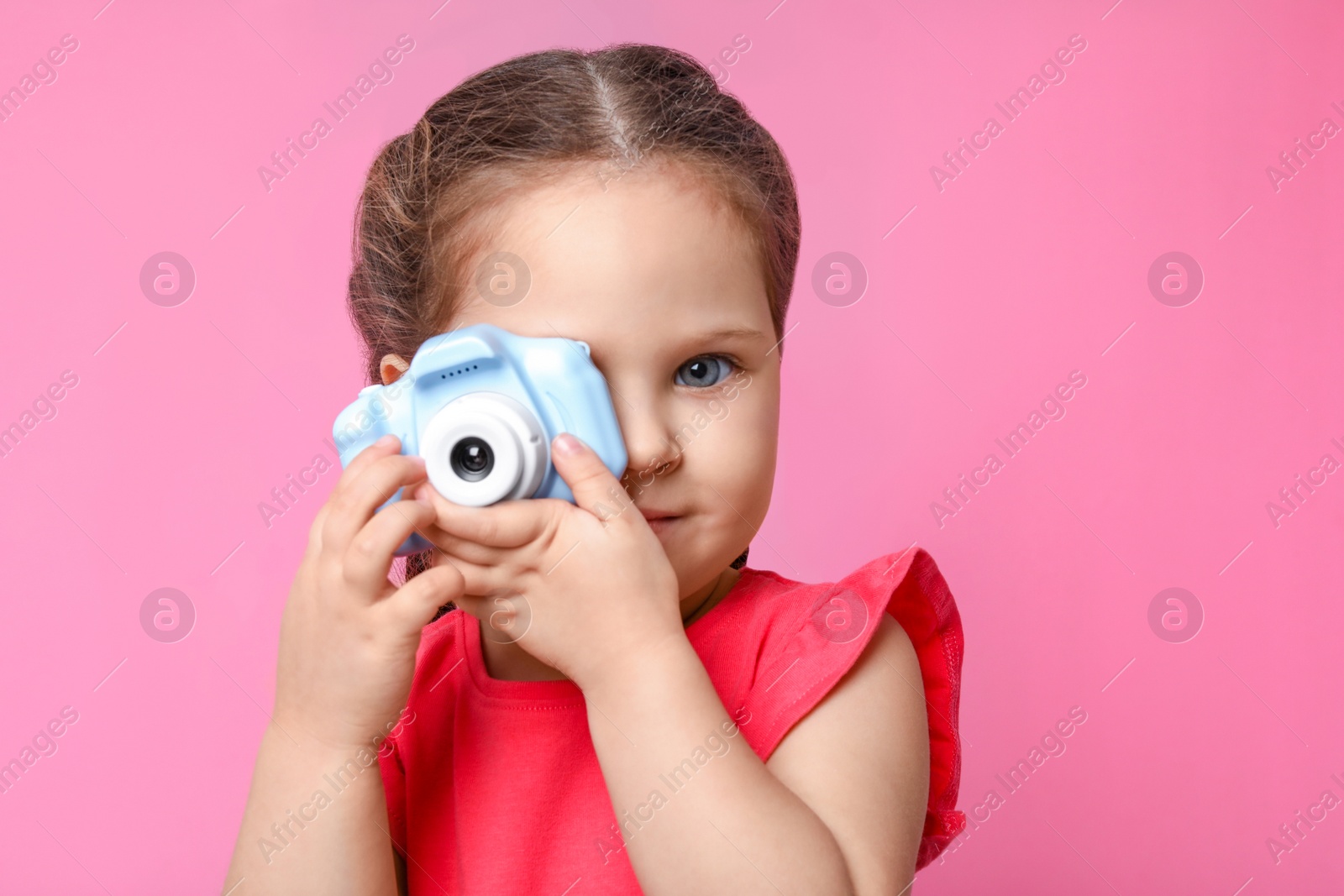 Photo of Little photographer taking picture with toy camera on pink background