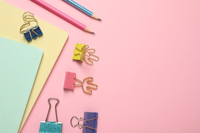 Photo of Binder clips and stationery on pink background, flat lay. Space for text