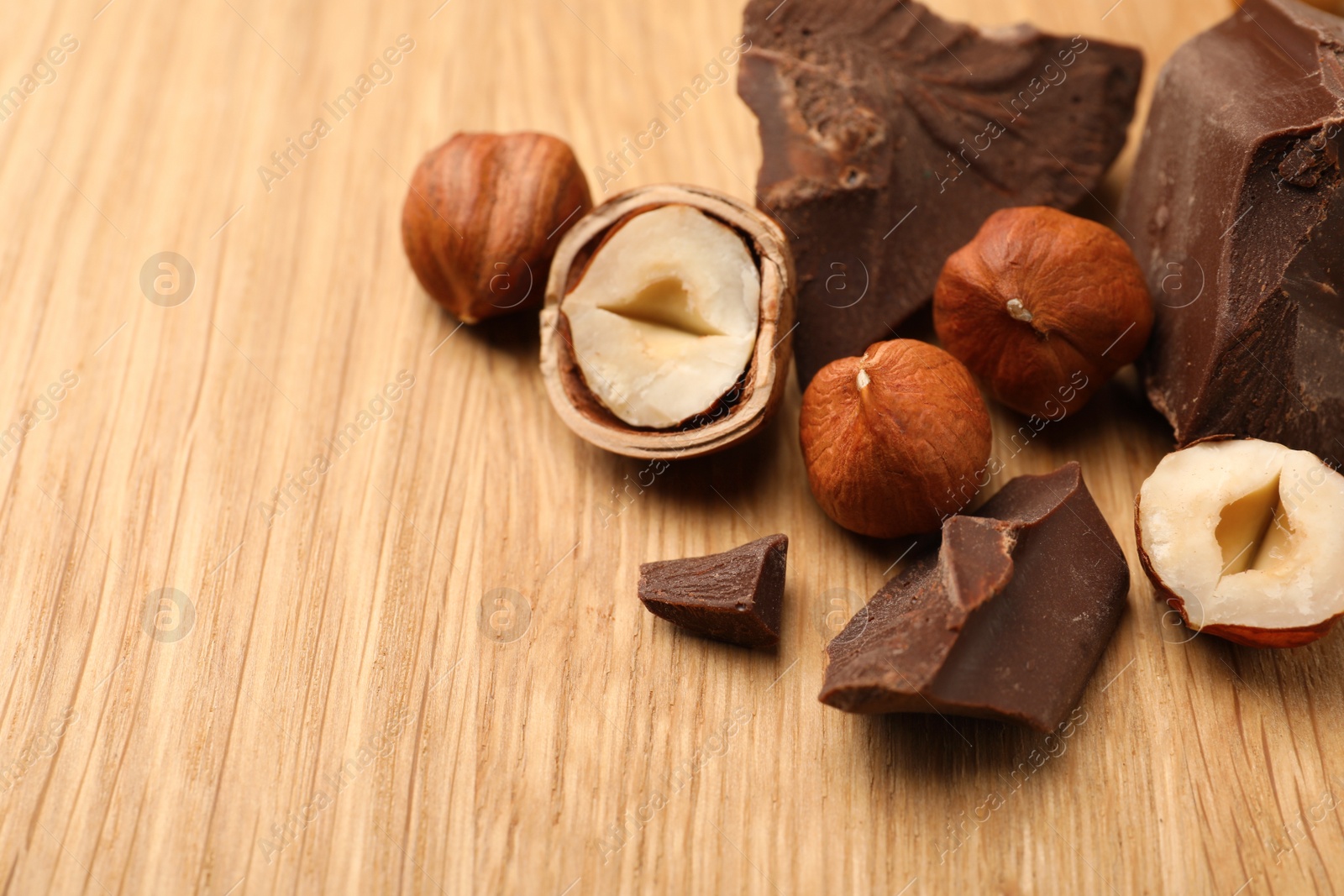 Photo of Delicious chocolate chunks and hazelnuts on wooden table, space for text