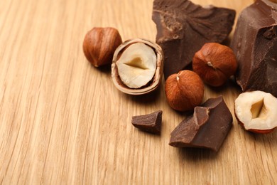 Delicious chocolate chunks and hazelnuts on wooden table, space for text