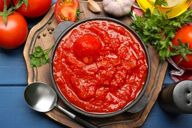 Photo of Homemade tomato sauce in bowl, spoon and ingredients on blue wooden table, flat lay