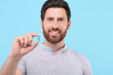 Photo of Handsome man with pill on light blue background, selective focus