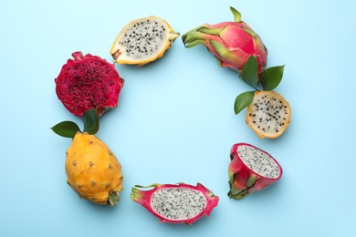 Photo of Frame of delicious cut and whole dragon fruits on light blue, flat lay. Space for text