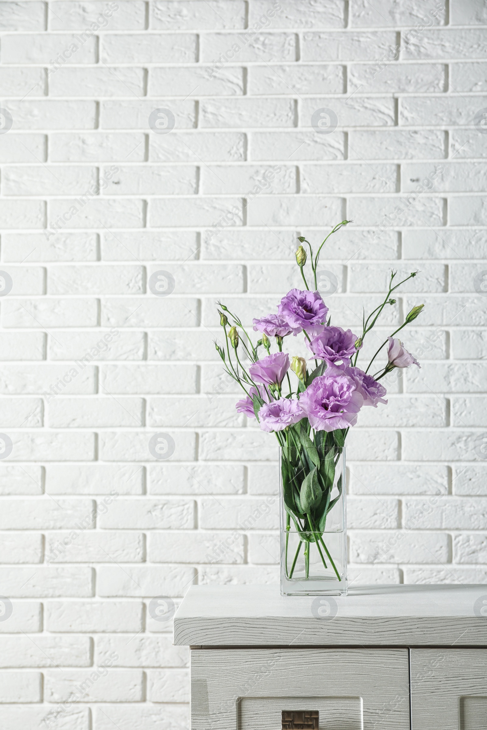 Photo of Vase with beautiful Eustoma flowers on table against brick wall