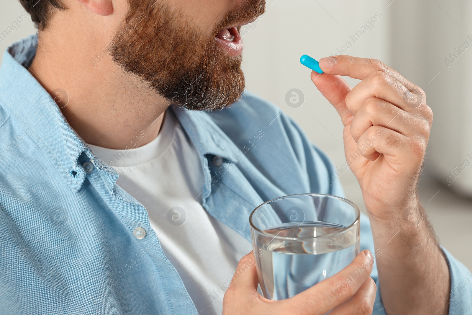 Photo of Man with glass of water taking pill on blurred background, closeup