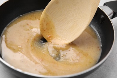 Photo of Stirring delicious turkey gravy in frying pan on table, closeup