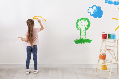 Little child painting on white wall indoors