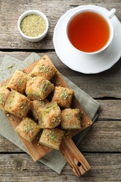 Photo of Delicious fresh baklava with chopped nuts and tea on wooden table, flat lay. Eastern sweets