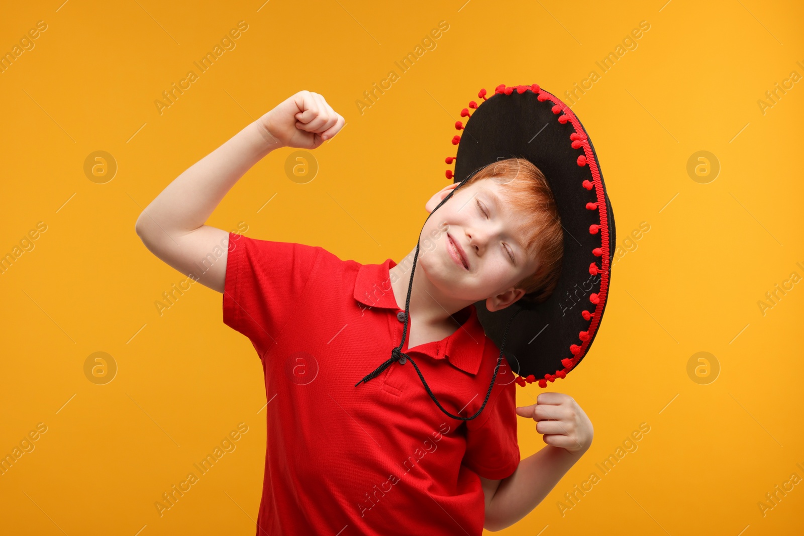 Photo of Cute boy in Mexican sombrero hat dancing on yellow background