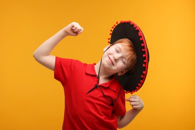Photo of Cute boy in Mexican sombrero hat dancing on yellow background
