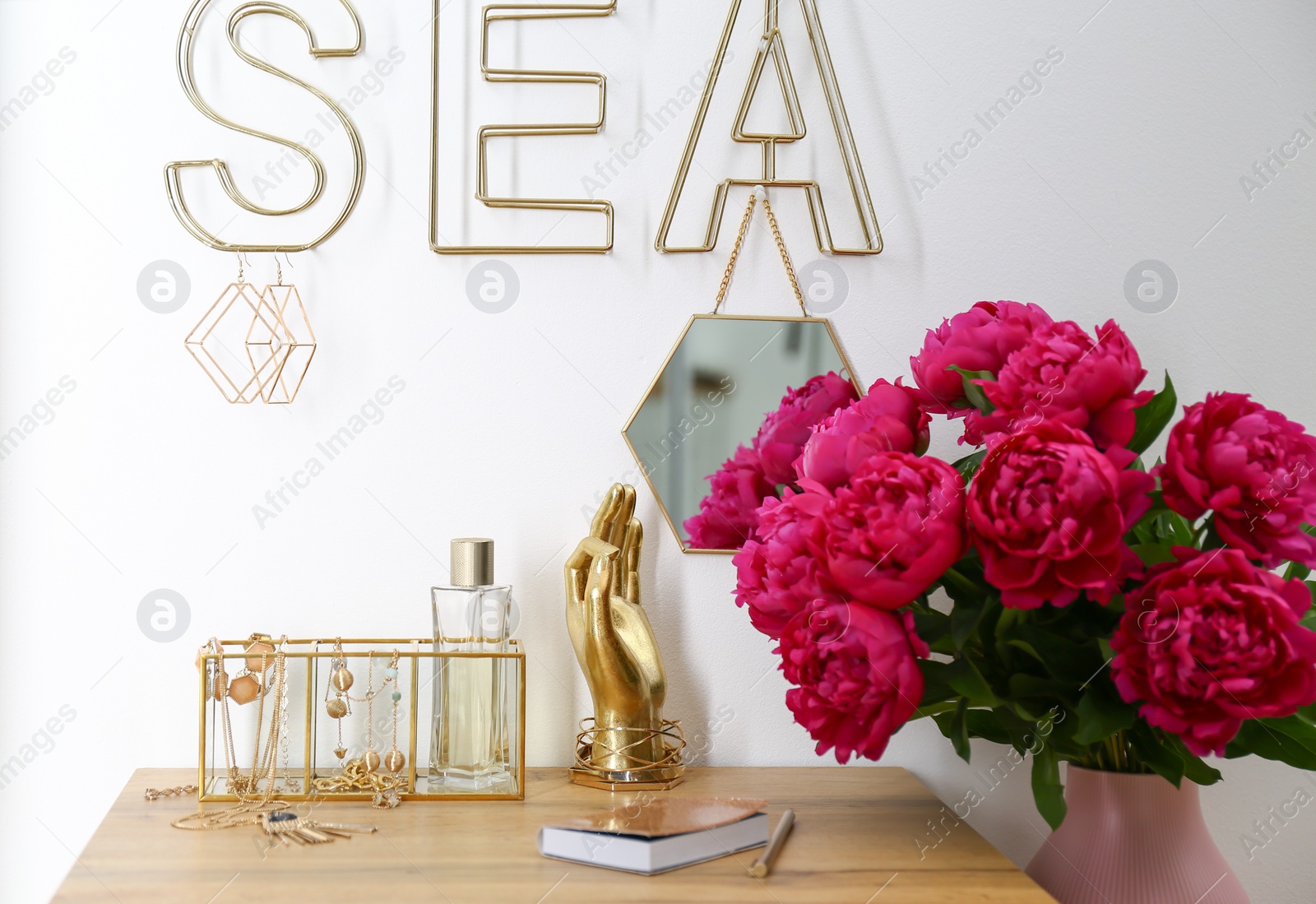 Photo of Composition with gold accessories and flowers on dressing table near white wall