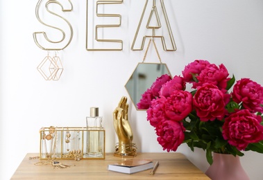 Composition with gold accessories and flowers on dressing table near white wall