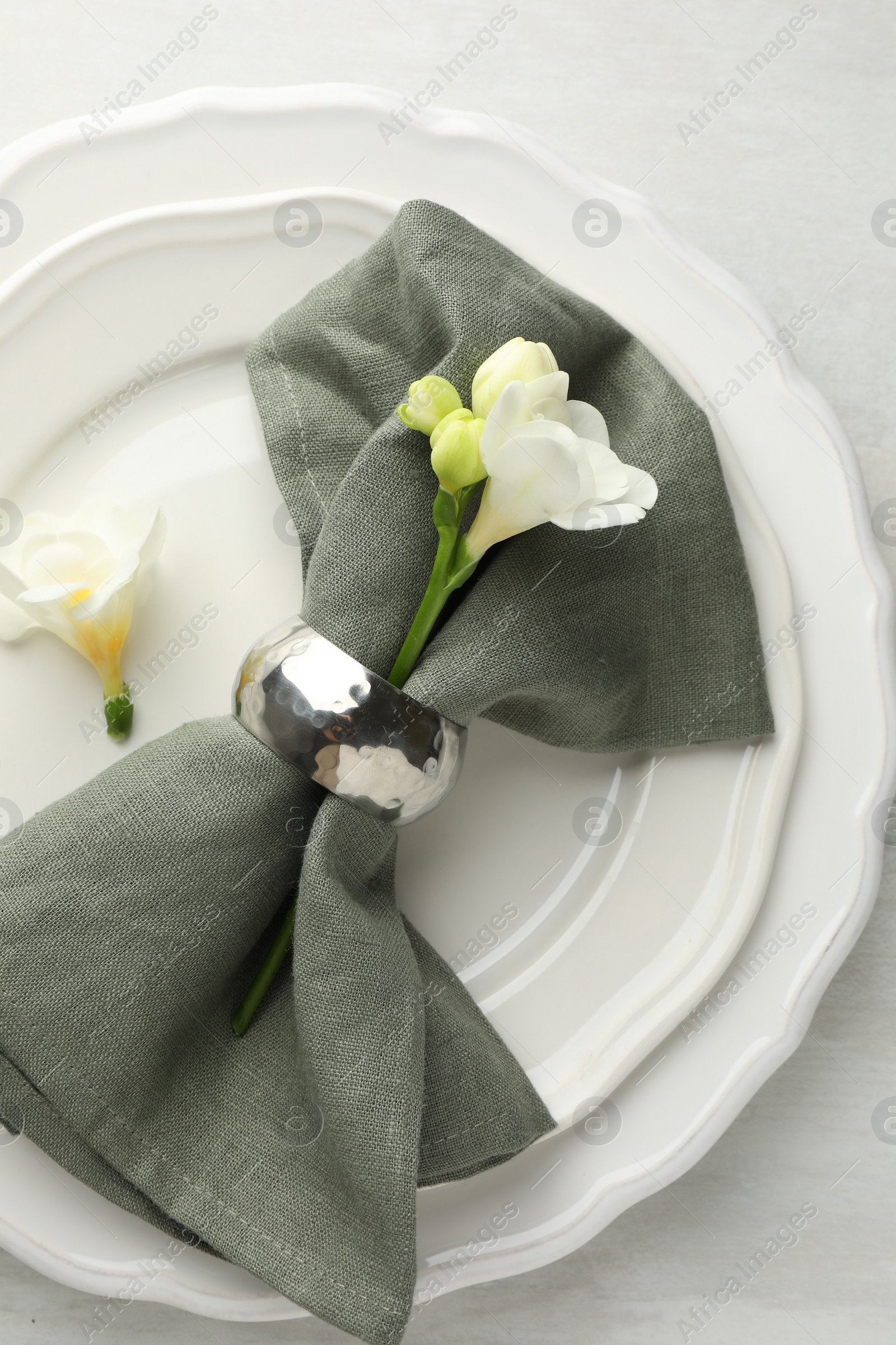 Photo of Stylish setting with napkin, flowers and plates on light textured table, top view