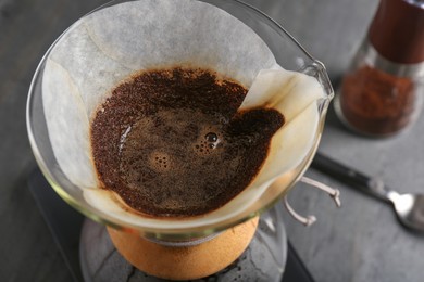 Photo of Glass chemex coffeemaker with paper filter and coffee on table, closeup