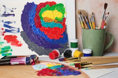 Photo of Abstract colorful painting and different artist's tools on textured table