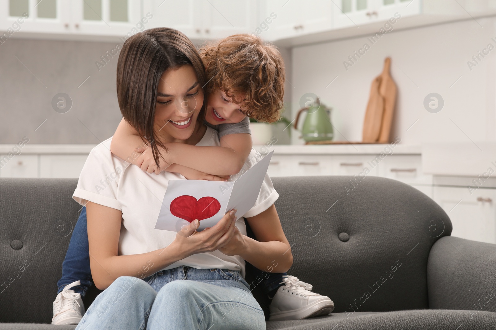 Photo of Little son congratulating his mom with Mother`s day at home. Woman holding greeting card