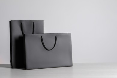 Black paper bags on white wooden table, space for text