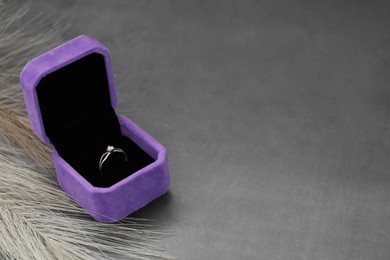 Photo of Jewelry box with stylish ring and feather on grey table. Space for text