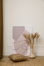 Fluffy reed plumes and painting near white wall indoors, space for text. Interior elements