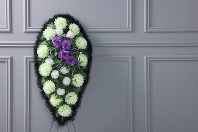 Photo of Funeral wreath of plastic flowers near light grey wall, space for text