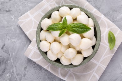 Tasty mozzarella balls and basil leaves in bowl on grey table, top view. Space for text