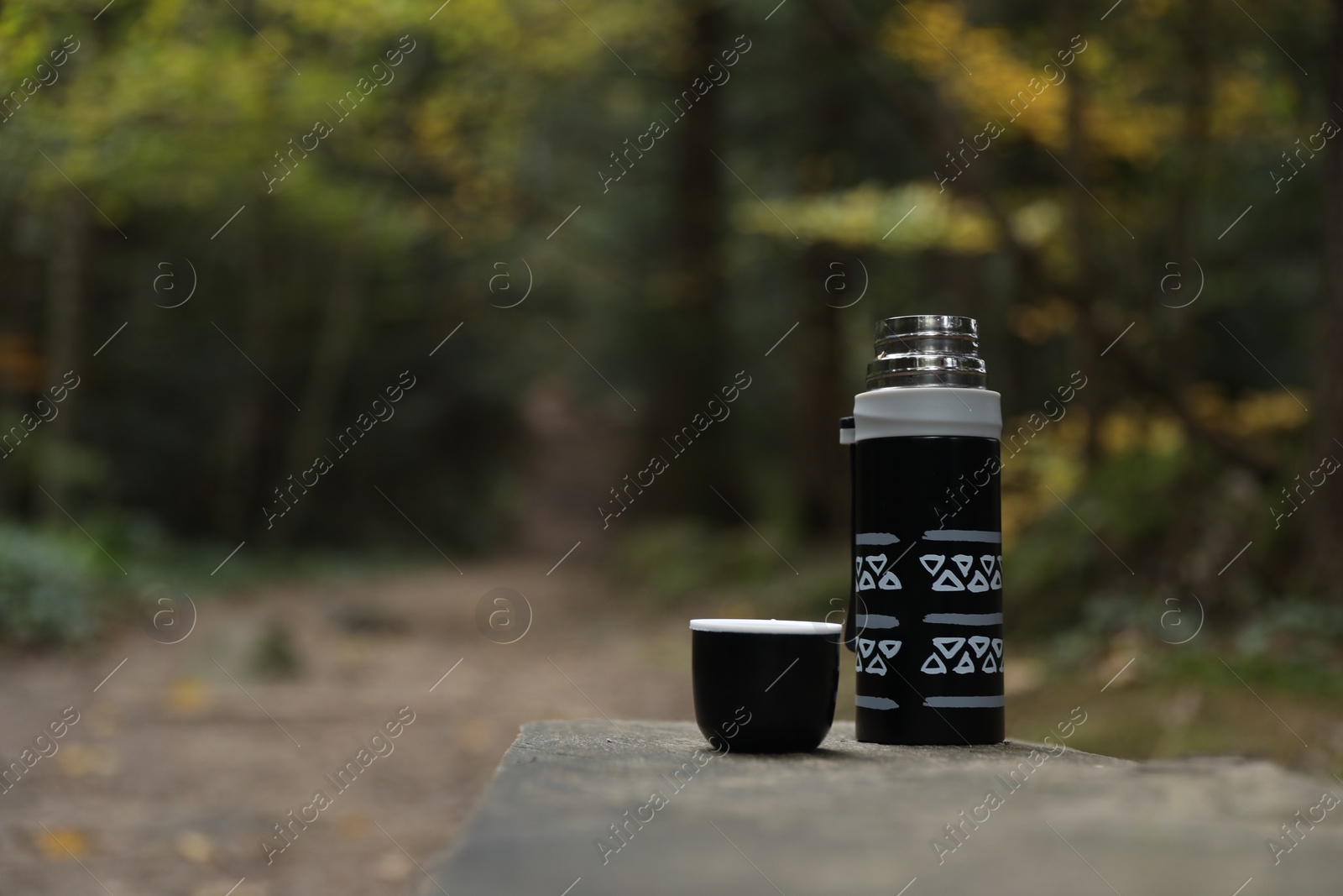 Photo of Black thermos and cup lid on wooden bench outdoors, space for text