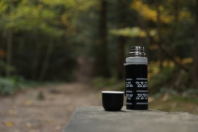 Photo of Black thermos and cup lid on wooden bench outdoors, space for text