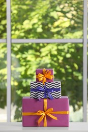 Stack of beautifully wrapped gift boxes on white table  near window. Space for text