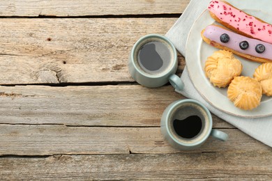 Aromatic coffee in cups, tasty eclairs and profiteroles on wooden table, top view. Space for text