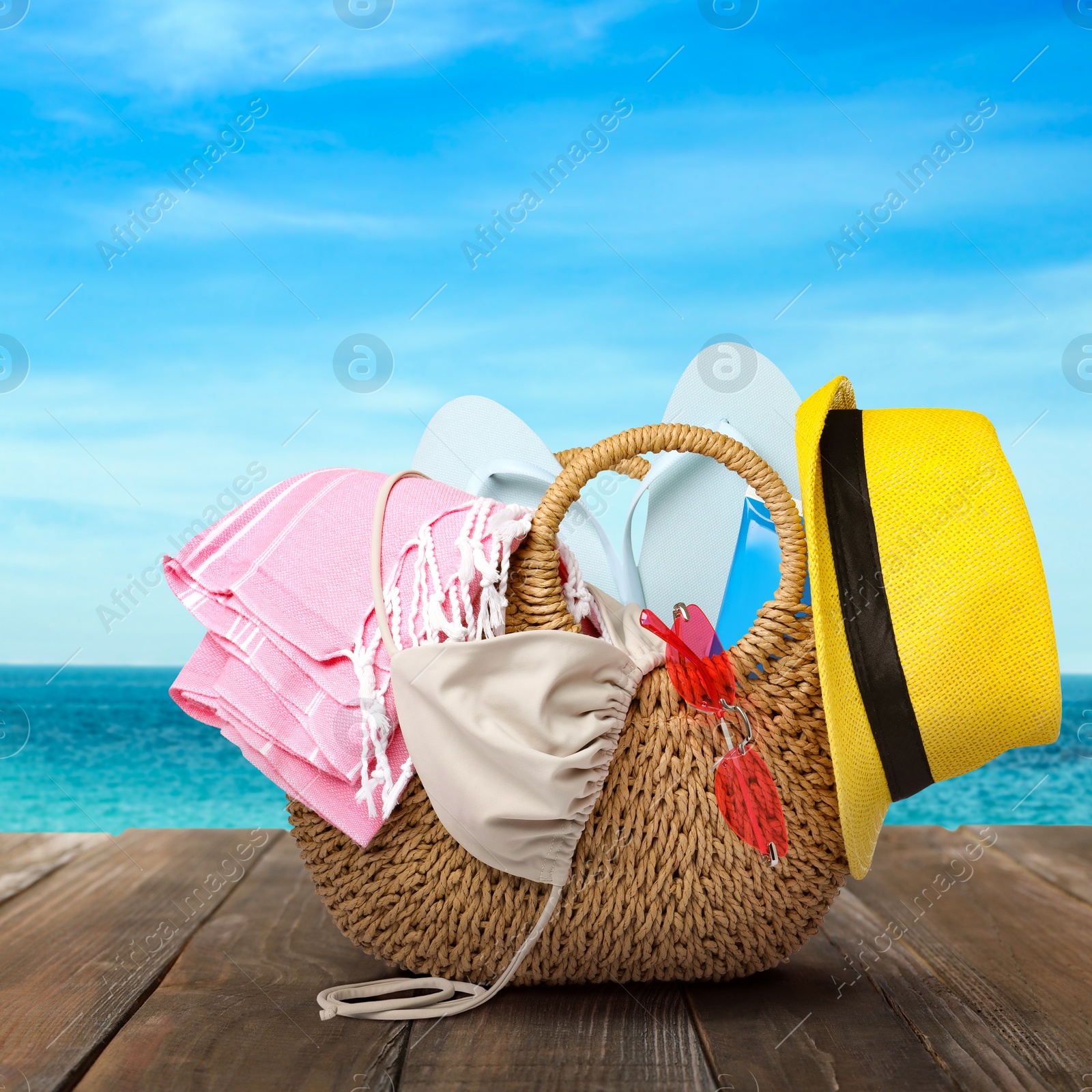 Image of Stylish bag with beach accessories on wooden surface near seashore 