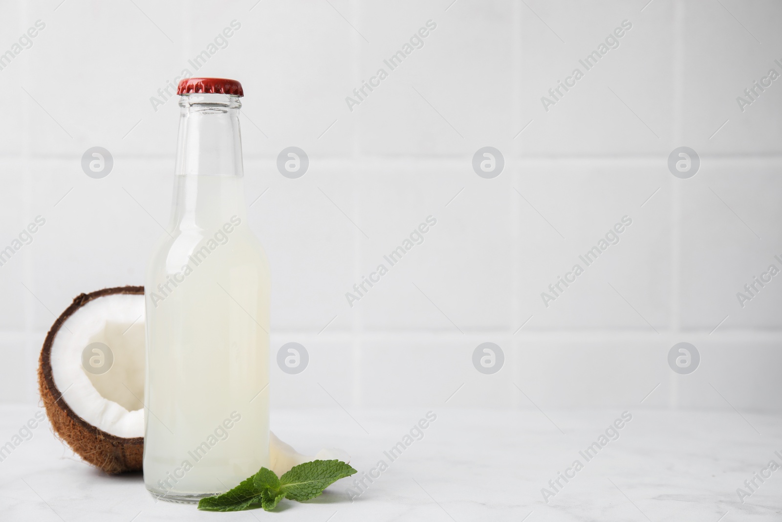 Photo of Delicious kombucha in glass bottle, coconut and mint on white marble table, space for text