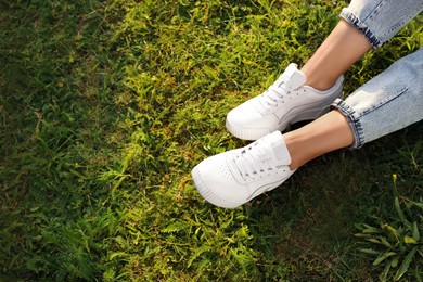 Photo of Woman in jeans and white shoes relaxing on green grass, closeup. Space for text