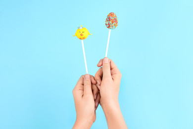Photo of Woman with delicious cake pops on light blue background, closeup. Easter holiday