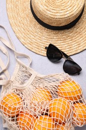 Photo of String bag with oranges, sunglasses and straw hat on grey table, top view