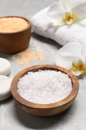 Photo of Natural sea salt in bowls, spa stones and flowers on grey marble table, closeup