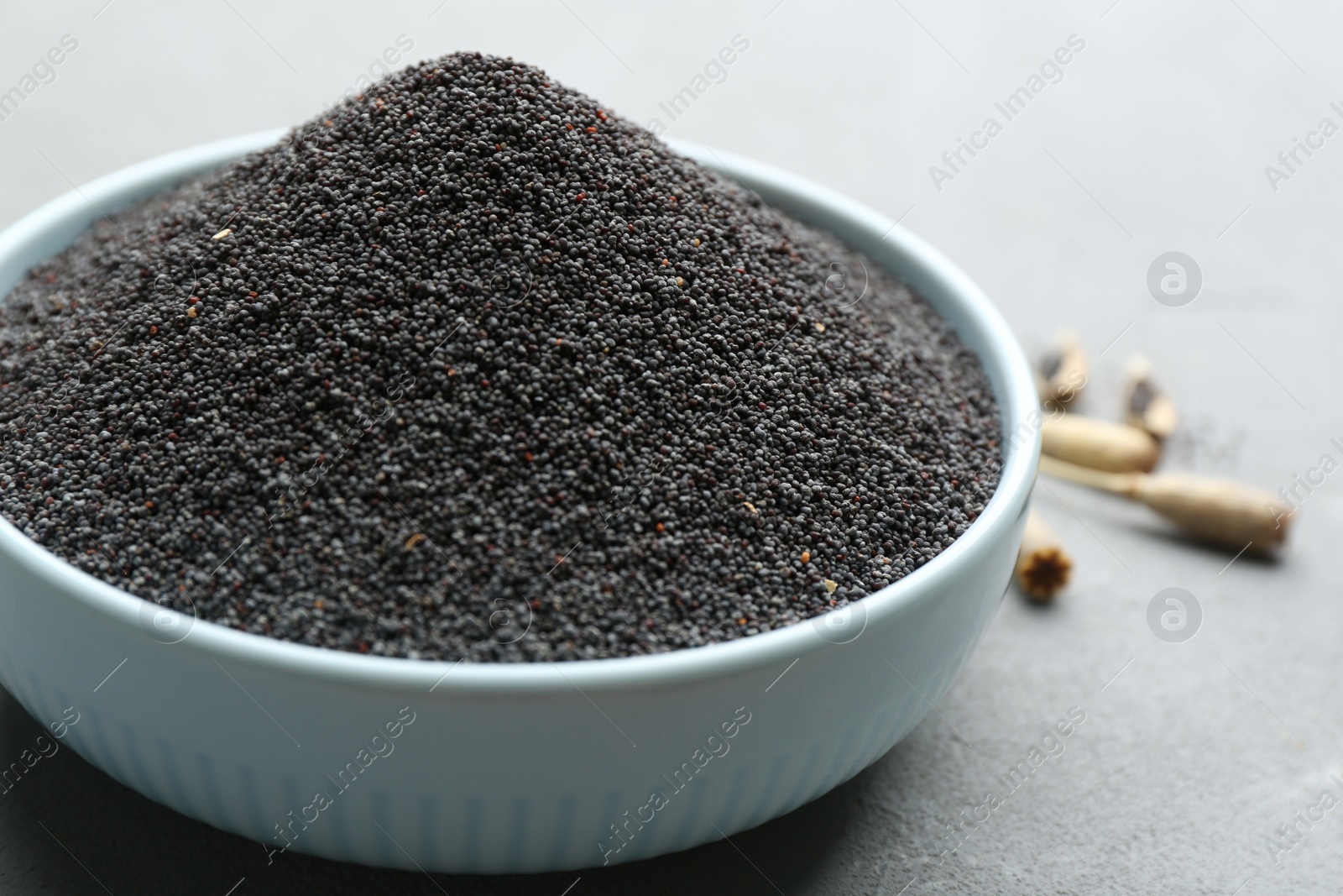 Photo of Poppy seeds in bowl on grey table, closeup