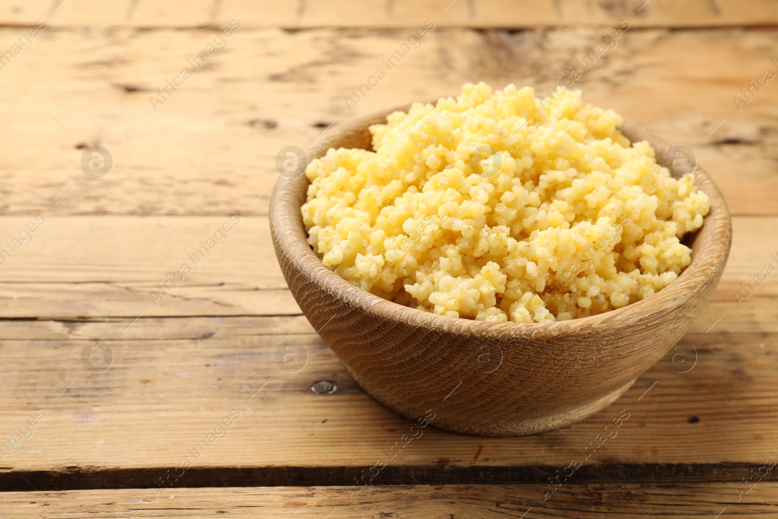 Photo of Tasty millet porridge in bowl on wooden table, closeup. Space for text