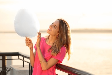 Happy young woman with cotton candy on waterfront