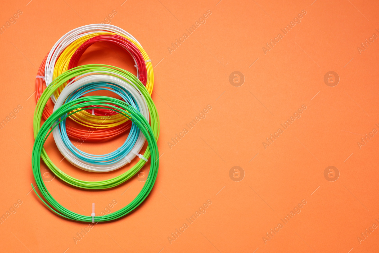 Photo of Colorful plastic filaments on orange background, flat lay. Space for text