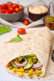 Photo of Delicious hummus wrap with vegetables on table