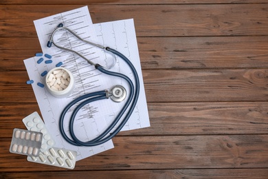 Photo of Flat lay composition with stethoscope and pills on wooden background. Cardiology service