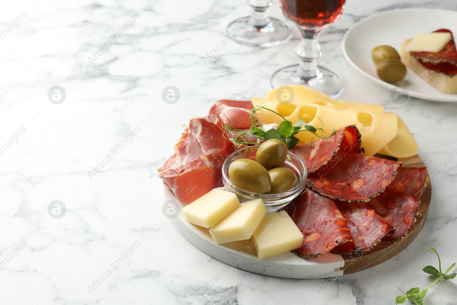 Photo of Serving board with delicious cured ham, cheese, sausage and olives on white marble table, space for text