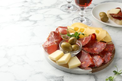 Photo of Serving board with delicious cured ham, cheese, sausage and olives on white marble table, space for text